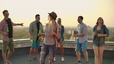 The-russian-blonde-is-dansing-on-the-roof-with-her-five-friends.-She-enjoys-this-time-with-beer-and-good-mood.-She-is-wearing-in-fashionable-hat-ripped-jeans-white-shirt-and-red-plaid-T-shirt.